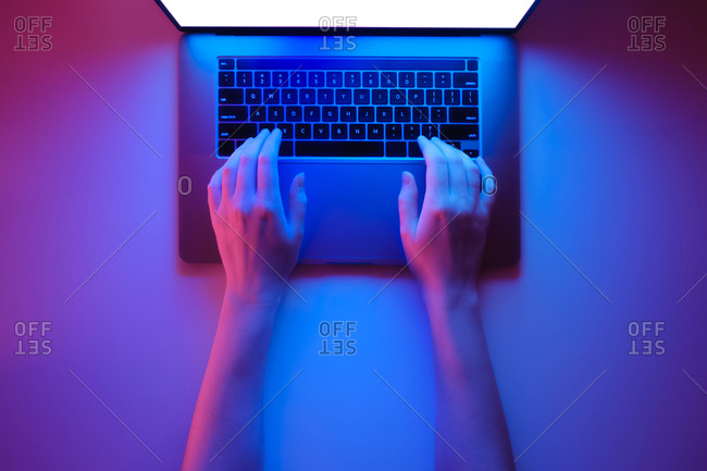 Hands on a modern laptop keyboard, top view in bright red and bl