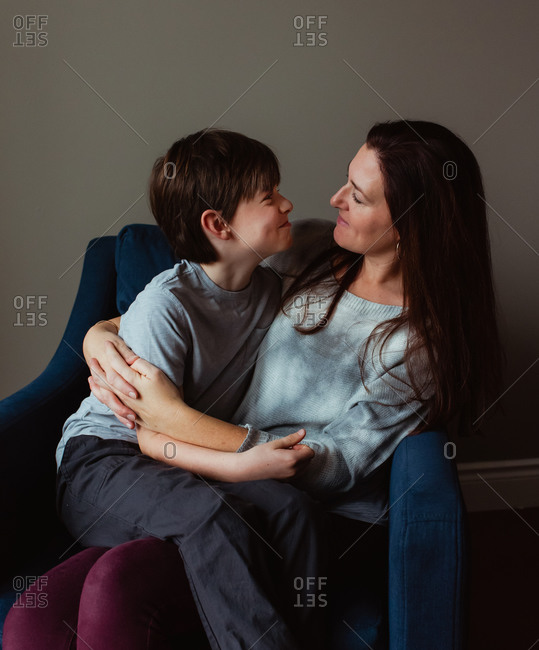 Happy woman hugging her son as he sits in her lap on a chair.