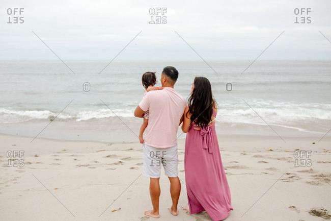 Asian couple with young child standing on beach gazing out at ocean