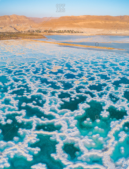 Aerial view of salt texture with veins in the shallow water of the Dead sea and mountains in the horizon.
