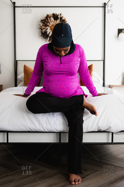 Pregnant Muslim Woman does bedside maternity yoga and stretches at home