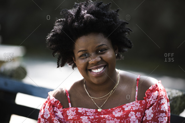Close up portrait of a black lady in a red floral dress smiling at the camera