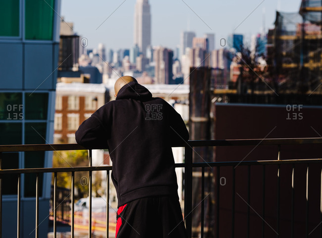 Bald man looking over a balcony while leaning against the fence