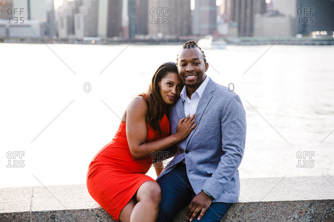 Woman leans over her boyfriend fondly sitting by a waterfront dressed in smart formals