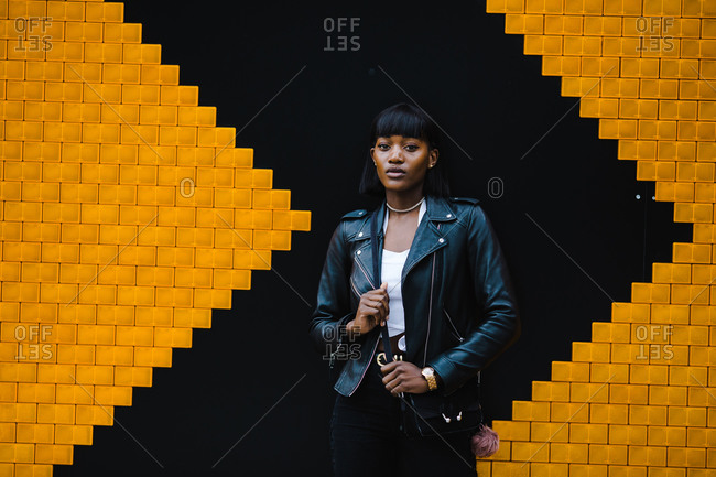 Black woman wearing a leather jacket posing in front of a black and yellow wall