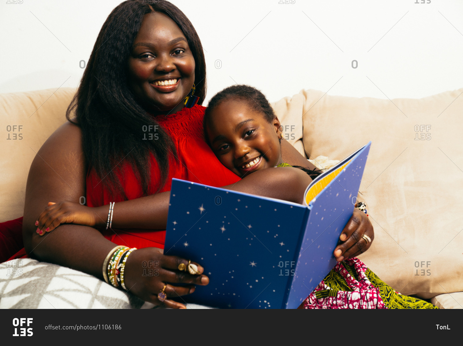Young girl hugging her black mother who is reading a bedtime stories book for her daughter