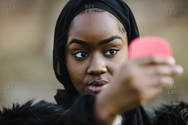 A closeup of a black woman wearing black headwrap looking at a mirror