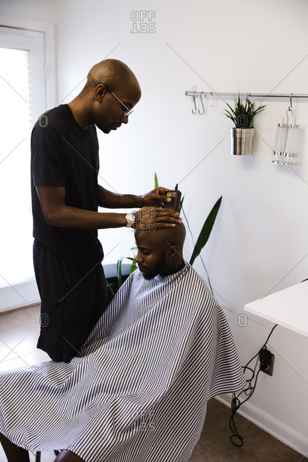 Vertical shot of a barber shaving a male client's head using a trimmer