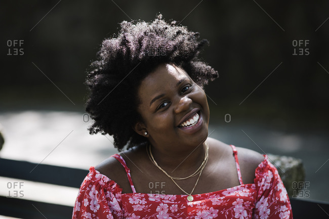 Close up portrait of a black lady in a red floral dress tilting her head and smiling at the camera