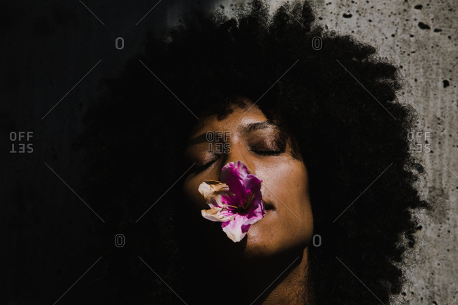 Black woman with afro and her eyes closed holding a purple flower in mouth