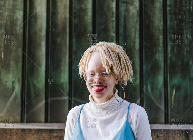 Horizontal portrait of a black woman with locks standing on a sidewalk smiles at the camera