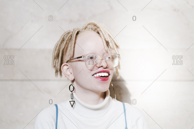 Horizontal head and shoulder portrait of a smiling albino woman in front of a wall