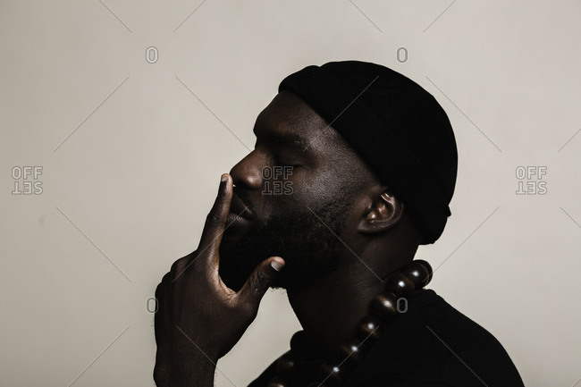 A side profile close up shot of a African American man with beard wearing a black beanie cap posing with a big beads necklace