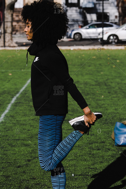 Vertical shot of a black athletic woman with curly hair stretching her legs on a grass field