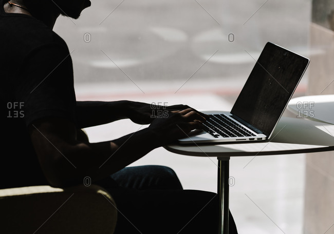A side view of a black man typing on a laptop