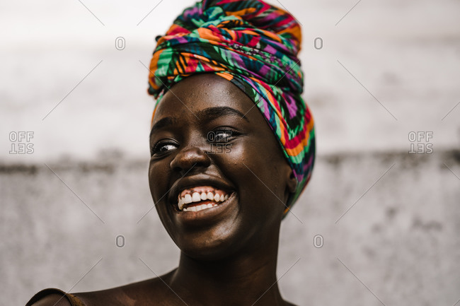 A close up shot of an African lady laughing in a multicolored headwrap