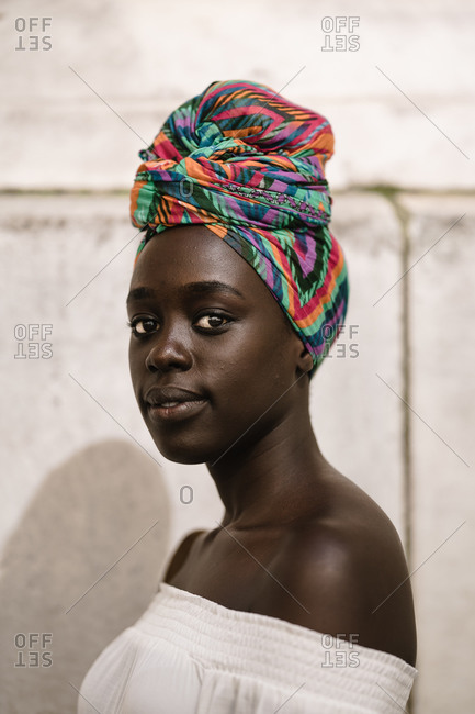 A close up portrait shot of a dark skin black woman in a white off-shoulder blouse standing against a wall