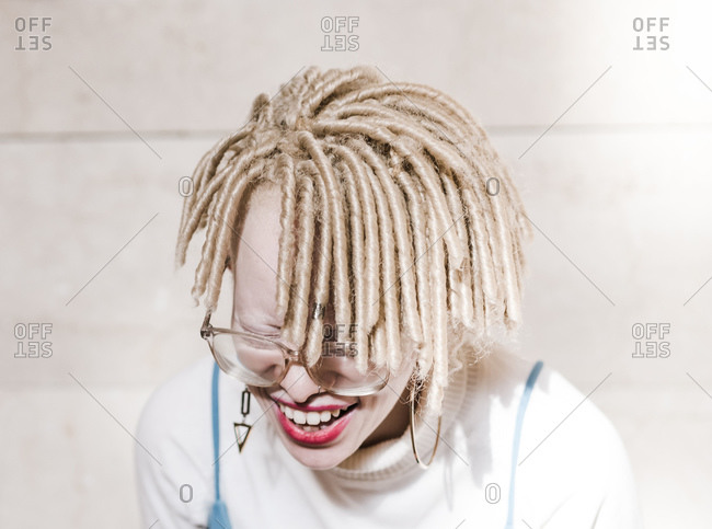 Horizontal head and shoulder portrait of an albino woman in delirious laughter in front of a wall