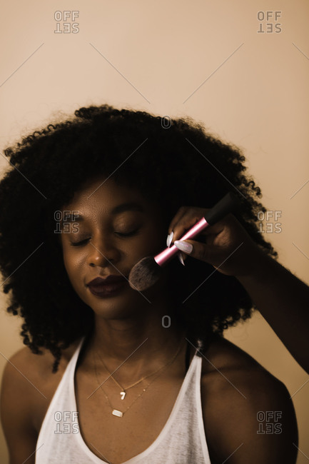 Vertical shot of a woman with curly hair getting her make up done in front of a brown wall