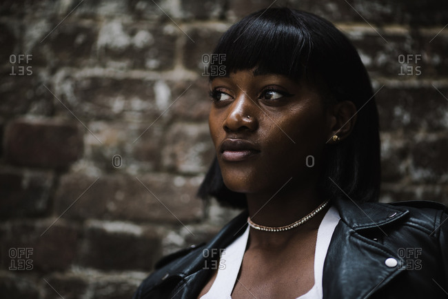 Close up portrait of a black woman wearing a leather jacket posing in front of a brick wall