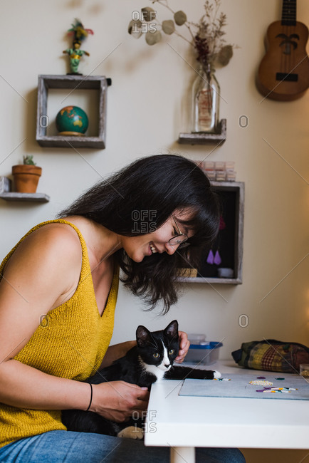 Vertical shot of a mixed race woman playing with her cat while making her own jewelry at home