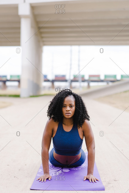 Vertical portrait of a strong focused woman performing cobra yoga pose outdoors