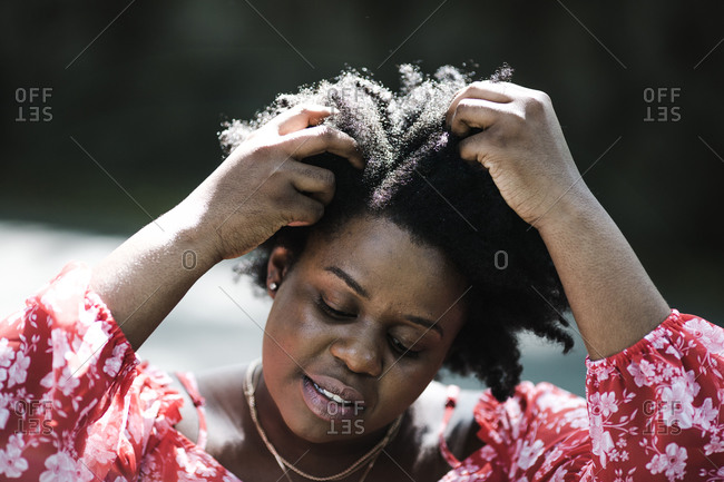 Close up portrait of a black lady in a red floral dress playing with her curls