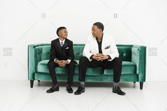 Horizontal portrait of a son and father sitting on a couch in suit look at each other