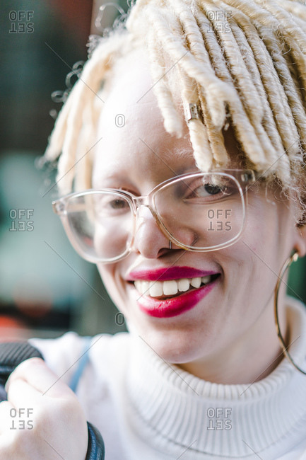Vertical headshot of a joyous woman with faux locs and glasses looking at the camera