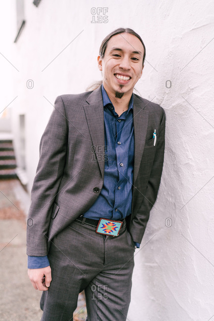 Three quarter length shot of a businessman leaning over a white wall smiles at the camera