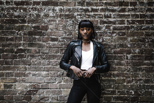 Black woman wearing a leather jacket posing in front of a brick wall