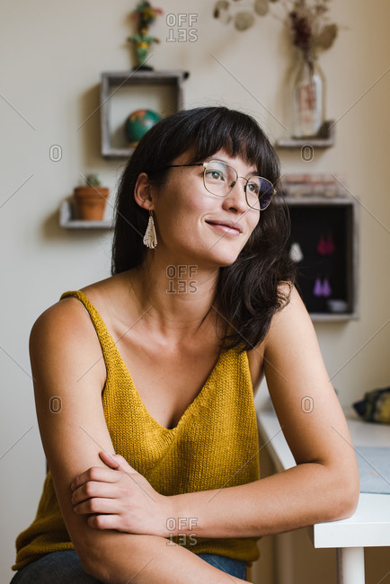Confident young mixed race jewelry designer sitting by her desk at home and looking away from the camera