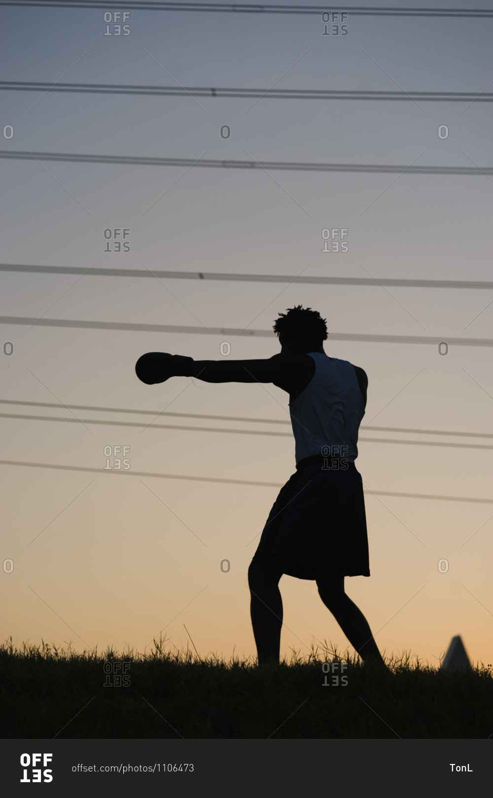 Silhouette of a black man boxing in the evening on a grassy field