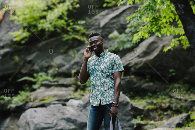 Horizontal shot of a man talking over cell phone outdoors in rocky terrain smiles at the camera