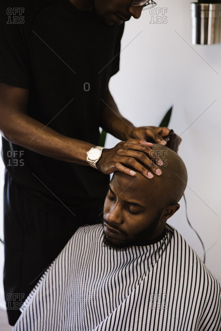 Barber shaving a male client's head using a trimmer