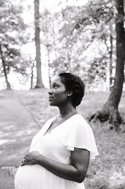 Monochrome shot of a pregnant black woman holding her belly and gazing up into the sky in the woods