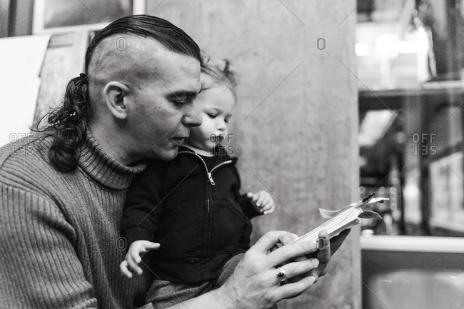 Black and white portrait of an American Indian and Alaska native father holding his daughter in arms and leafing through a booklet