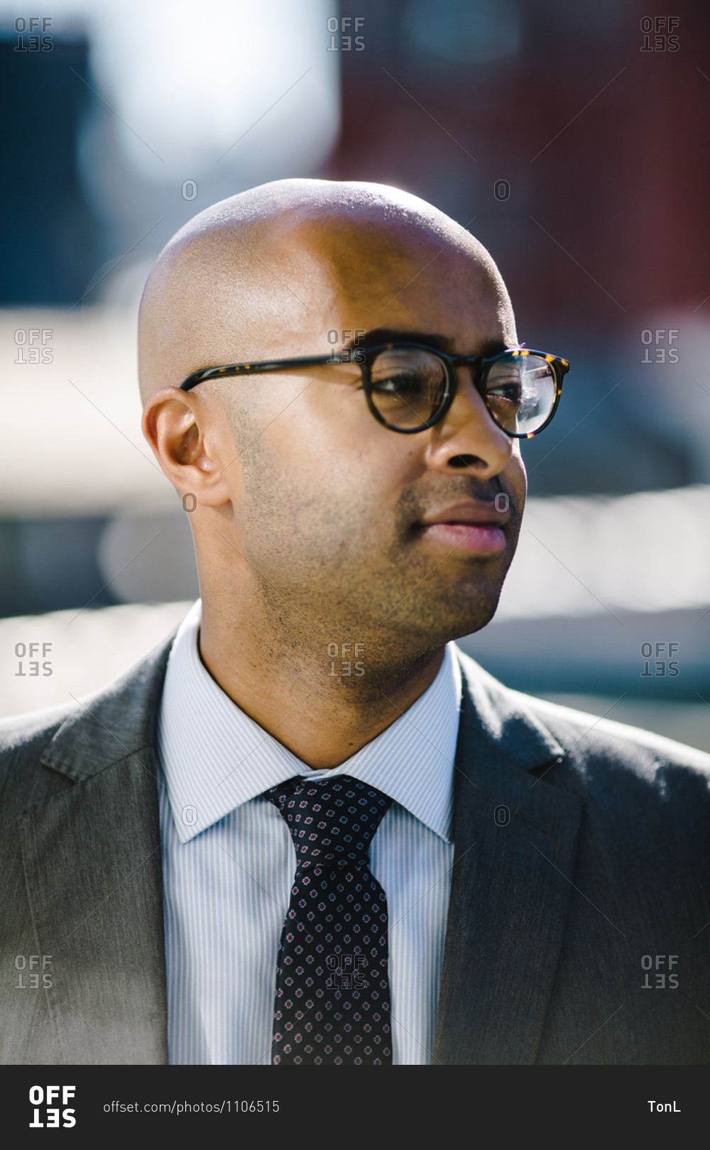 Portrait of a bald black man in a suit and glasses looking off into the distance