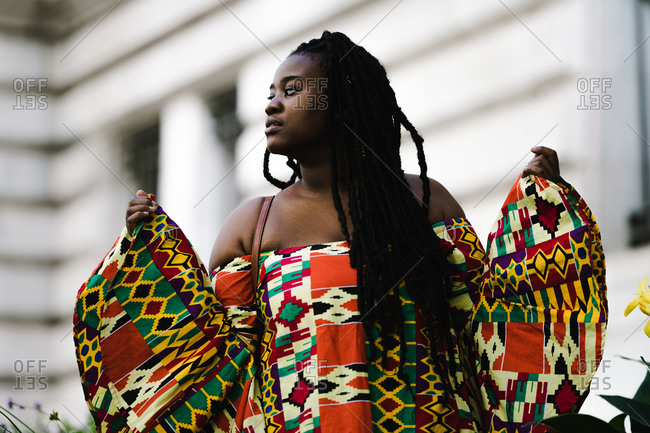 A medium shot of a black woman in a colorful African dress with long braids looking sideways