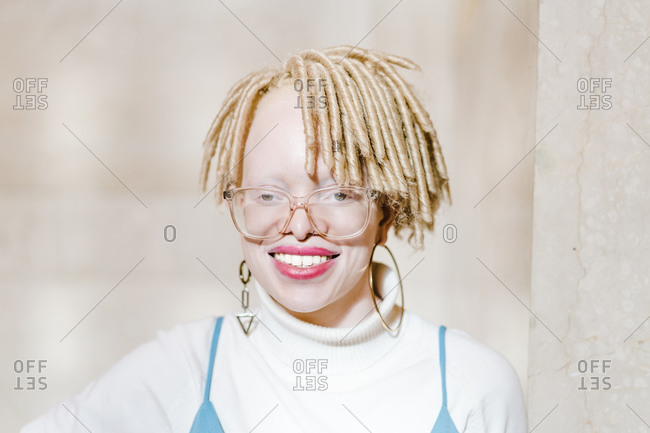 Horizontal head and shoulder portrait of a joyous albino woman smiling at the camera in front of a wall