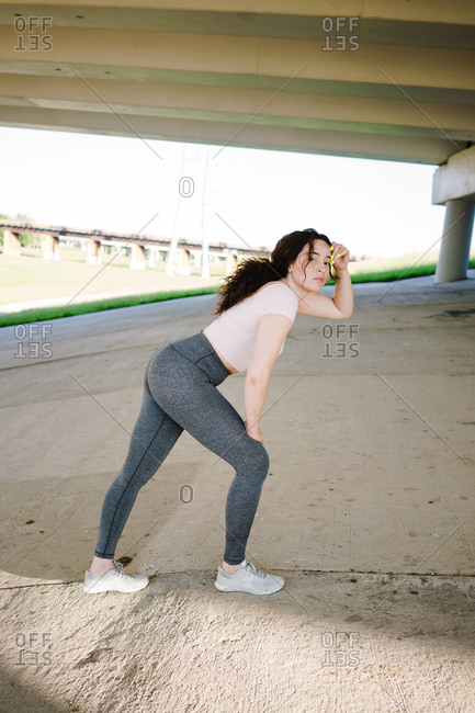 Young woman posing while stretching on the slope under the bridge