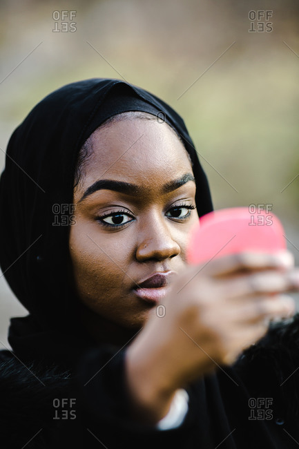 A close up portrait shot a black woman looking at herself in a compact mirror