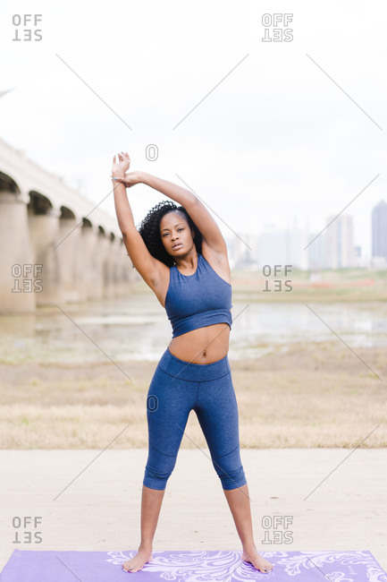 Side shot of a Strong focused woman standing in the middle of the road and performing yoga outdoors