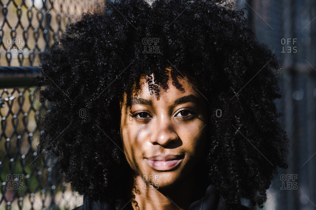 Portrait of a black athletic woman with curly hair standing next to a metallic fence