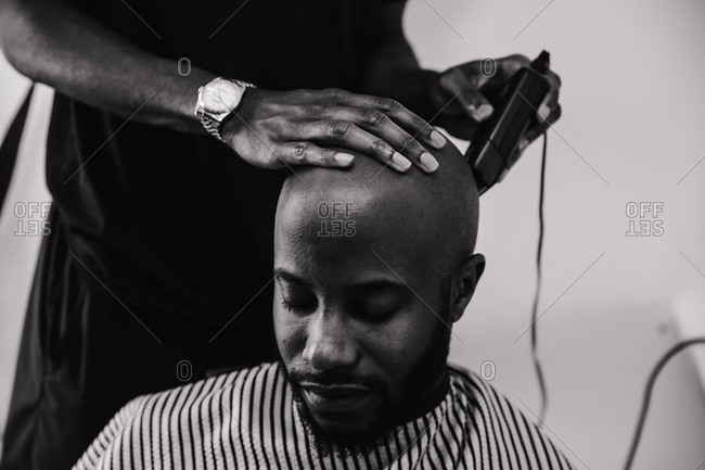 Black and white shot of the close up of a barber shaving a male client's head using a trimmer