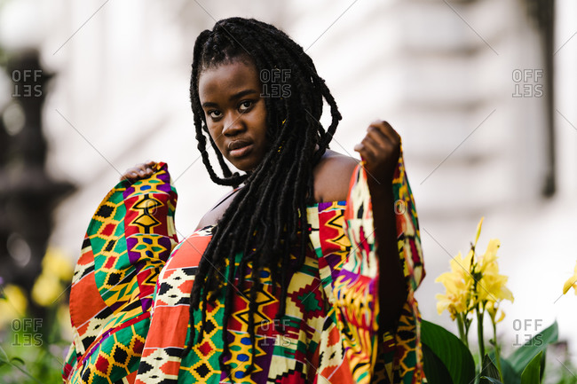 A medium shot of a black woman in a colorful African dress with long braids giving a stylish pose