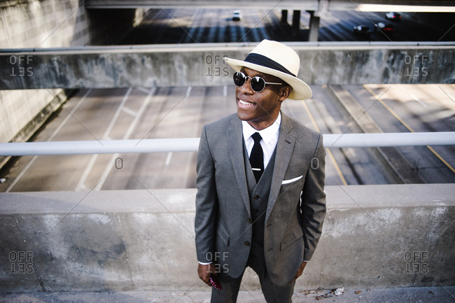 Black man in a gray suit with sunglasses and tan hat looking up