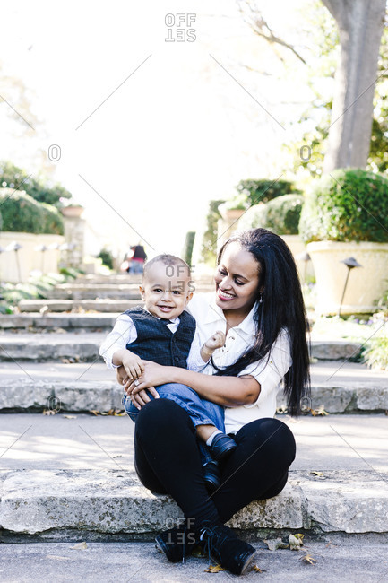 Vertical portrait of a joyous mother sitting with her little son in lap outdoors