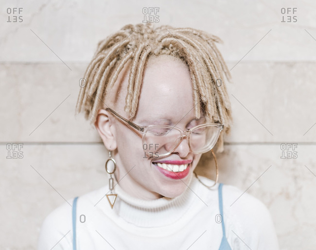 Horizontal head and shoulder portrait of a joyous albino woman with eyes closed in front of a wall