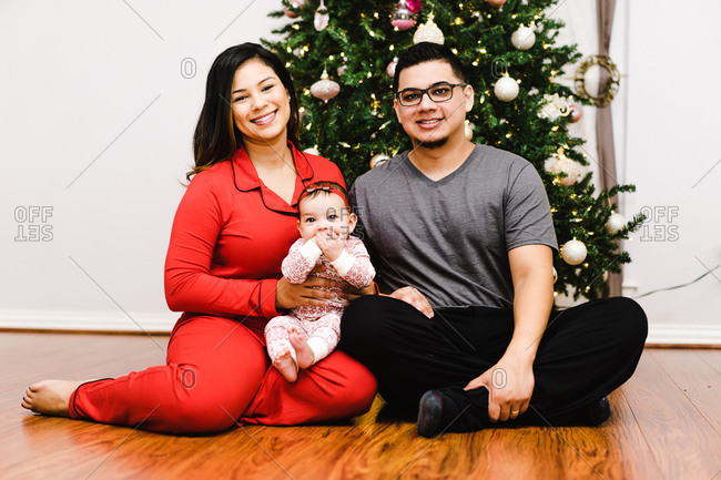 Horizontal shot of a joyous latino family with daughter sitting in front of a Christmas tree on the floor